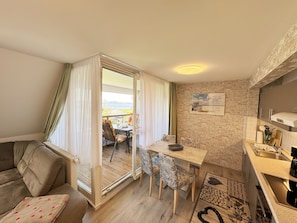 A cozy living room with a sofa, a dining table with chairs, a kitchen area with a sink, and a view of the outdoors through a sliding door. - Apartment 05 with balcony and view of the Bodden - MR: Haus Inselperle with view of the (Mönchgut)
