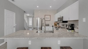 Una cocina moderna con armarios blancos, encimera de mármol y electrodomésticos de acero inoxidable.
