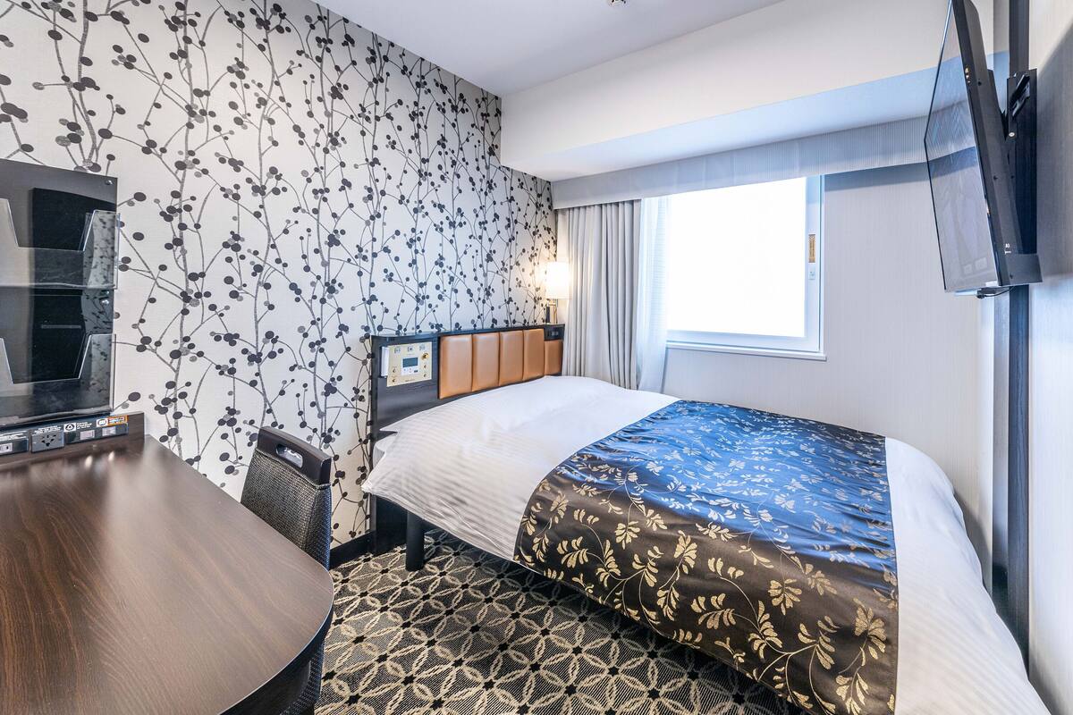 A hotel room with a bed, a desk, a chair, a TV, and a window with curtains.