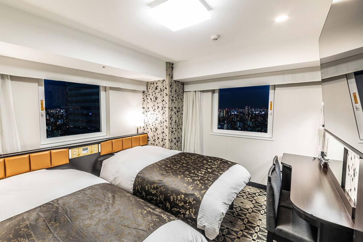 A hotel room with two beds, a desk, and a view of the city at night.