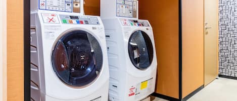 Two front-loading washing machines in a hotel room with wooden walls and a patterned floor.