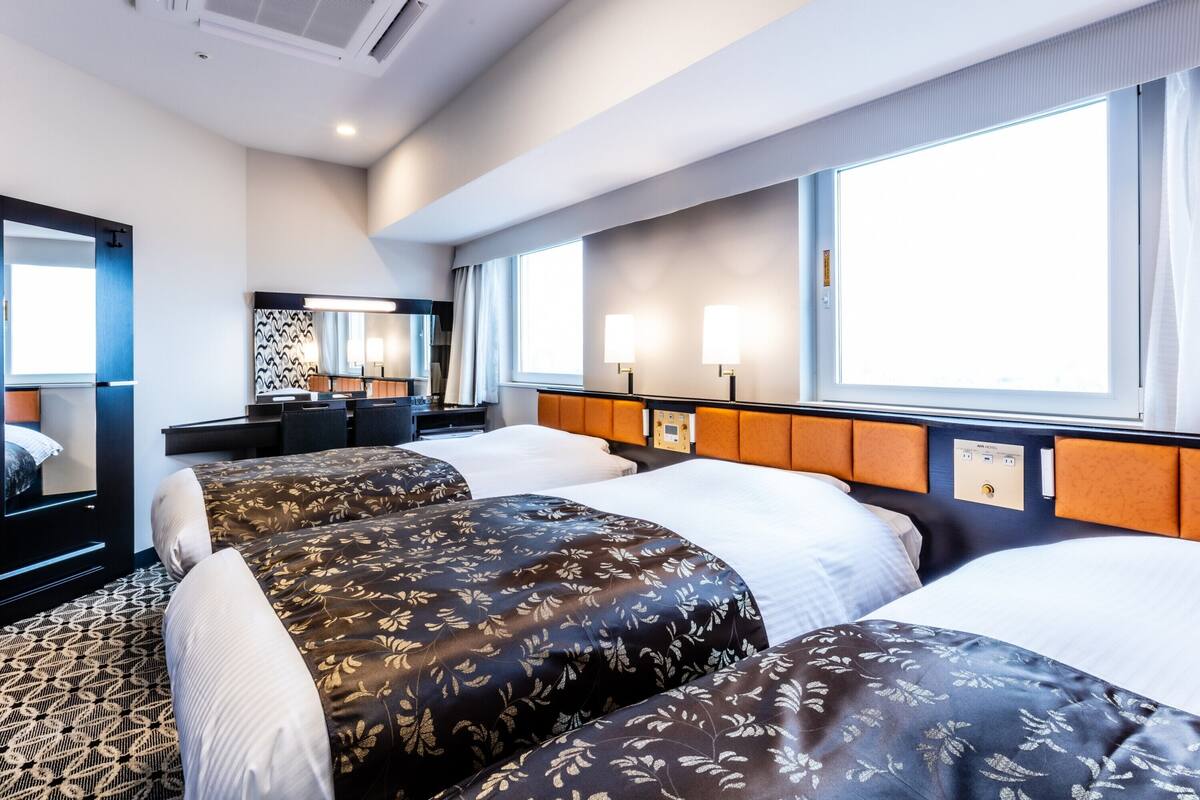 A hotel room with two beds, a desk, a chair, a mirror, and a window.