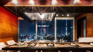 Un comedor moderno con vistas panorámicas de la ciudad, una mesa larga preparada para comer y sillas de mimbre.
