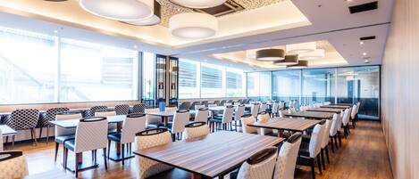 A modern dining area with multiple tables and chairs, large windows, and a patterned ceiling.