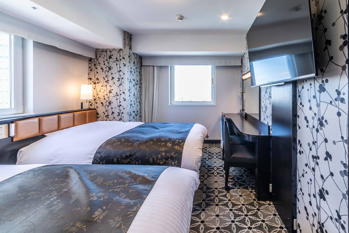 A hotel room with two beds, a desk, a TV, and a patterned carpet.