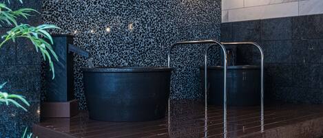 A spa area with a stone wall, two black tubs, and a metal bench.