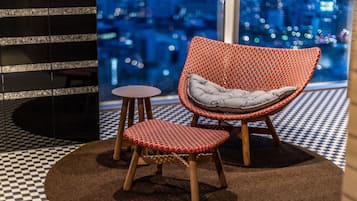 A red woven chair with a grey cushion and a matching stool, placed on a patterned rug.