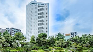 A modern high-rise building with a reflective glass facade, surrounded by lush greenery and a tranquil pond.