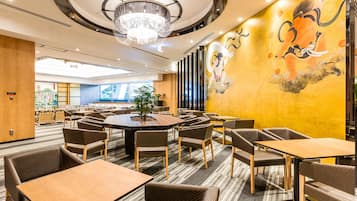 A modern hotel lobby with a large round table, multiple seating areas, and a mural on the wall.