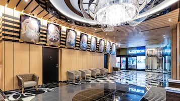 A modern hotel lobby with a checkered floor, a chandelier, and a row of framed artwork on the wall.