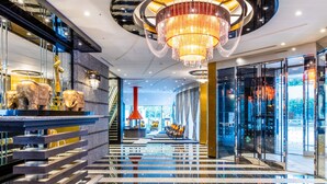 Un moderno vestíbulo de hotel con una gran araña, pisos de mármol y una escalera que conduce a los niveles superiores.
