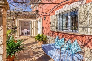 A cozy outdoor seating area with a metal bench and cushions, surrounded by potted plants and a stone pathway.