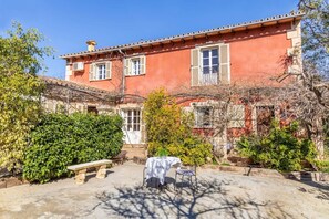 A red building with a courtyard, a bench, and a table with a cloth.