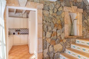 A kitchen with white cabinets, a tiled backsplash, and a stone wall.