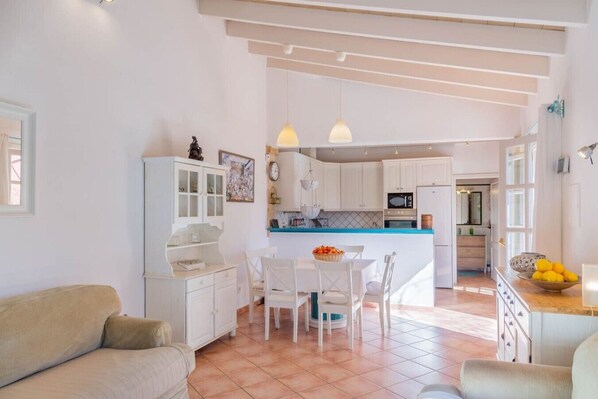 A modern kitchen with white cabinets, a dining area with a table and chairs, and a living room with a sofa. - Family Country House with Pool in Andratx (Port Andratx)