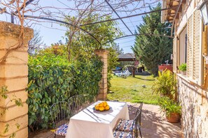 Une terrasse avec une table dressée pour deux personnes, entourée de verdure et bordée d’un mur de pierres.