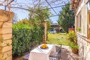 A patio with a table set for dining, surrounded by greenery and a view of a backyard with outdoor furniture.