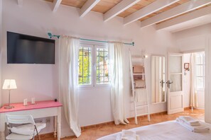 Une chambre à coucher avec un lit, un bureau avec une lampe, une chaise, un téléviseur fixé au mur et une fenêtre avec des rideaux.