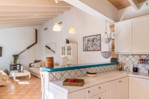 A kitchen with a blue countertop, white cabinets, hanging baskets, and a painting on the wall.