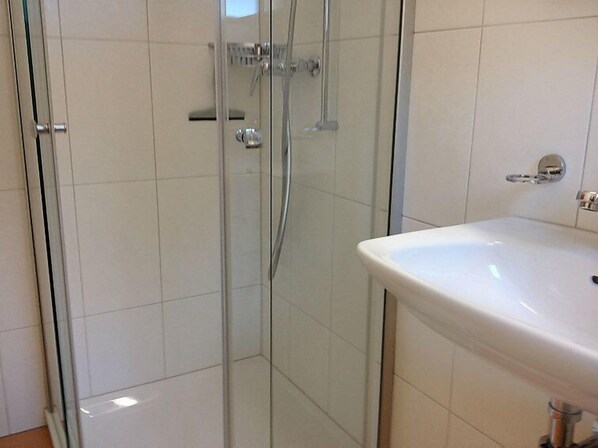 A bathroom with a glass shower enclosure, a white sink, and a tiled floor.