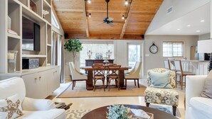 A spacious living area with a wooden ceiling, a dining table with chairs, a sofa, and a coffee table.