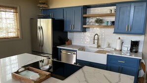 A modern kitchen with blue cabinets, a stainless steel refrigerator, a dishwasher, and a marble countertop.
