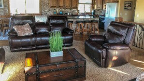 A spacious living room with leather sofas, a coffee table with a plant, and a kitchen in the background. - Amazing view - Lake House Retreat with Mountain Cabin Warmth (Garden City)