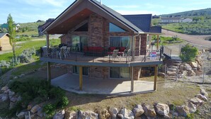 A two-story house with a stone facade, a balcony with outdoor furniture, and a large window. - Amazing view - Lake House Retreat with Mountain Cabin Warmth (Garden City)