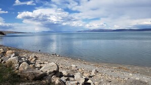 A calm lake with a rocky shoreline and distant mountains under a partly cloudy sky. - Amazing view - Lake House Retreat with Mountain Cabin Warmth (Garden City)