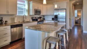 A modern kitchen with white cabinets, stainless steel appliances, granite countertops, and bar stools. - Ocean Adventure - Oyhut Bay Seaside Village (Ocean Shores)
