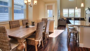 A dining area with a wooden table and wicker chairs, a kitchen with a bar area, and large windows with blinds. - Ocean Adventure - Oyhut Bay Seaside Village (Ocean Shores)