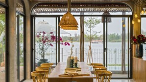 Un comedor con una mesa y sillas de madera, una lámpara colgante y vistas a una masa de agua a través de amplios ventanales.