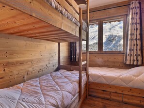 A wooden cabin room with bunk beds, a window with a snowy mountain view, and a curtain with a floral pattern. - Charming 3-room near slopes, pets allowed (Méribel)