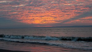 A sunset over the ocean with waves approaching the shore.