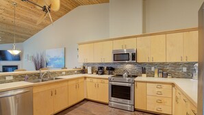 A modern kitchen with wooden cabinets, stainless steel appliances, and a herringbone tile backsplash.