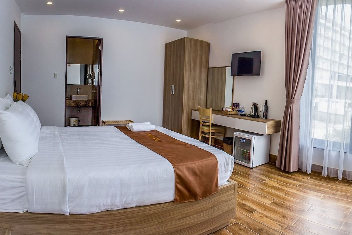 A hotel room with a large bed, a desk, a television, and a window with curtains.