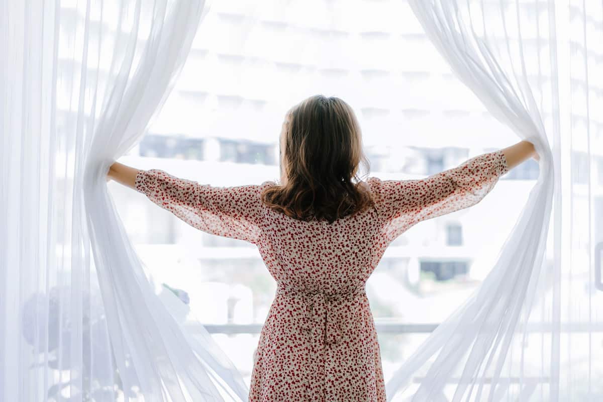 A person standing with arms outstretched in front of a sheer curtain.