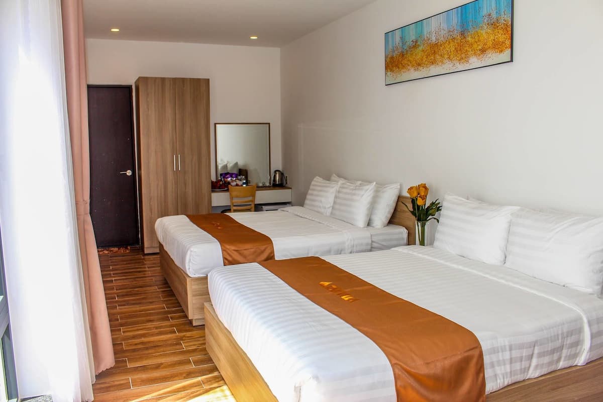 A hotel room with two beds, a wooden wardrobe, a desk with a chair, a mirror, and a painting on the wall.