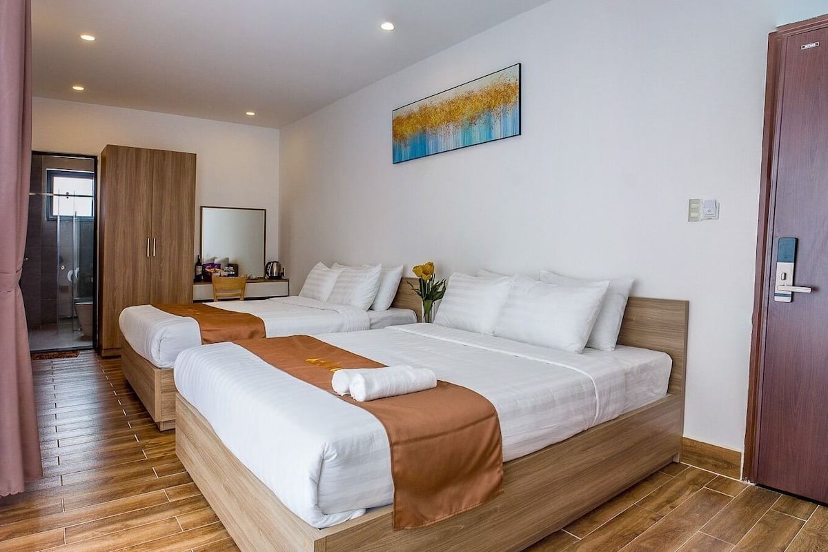 A hotel room with two beds, a wooden wardrobe, a painting, and a door.