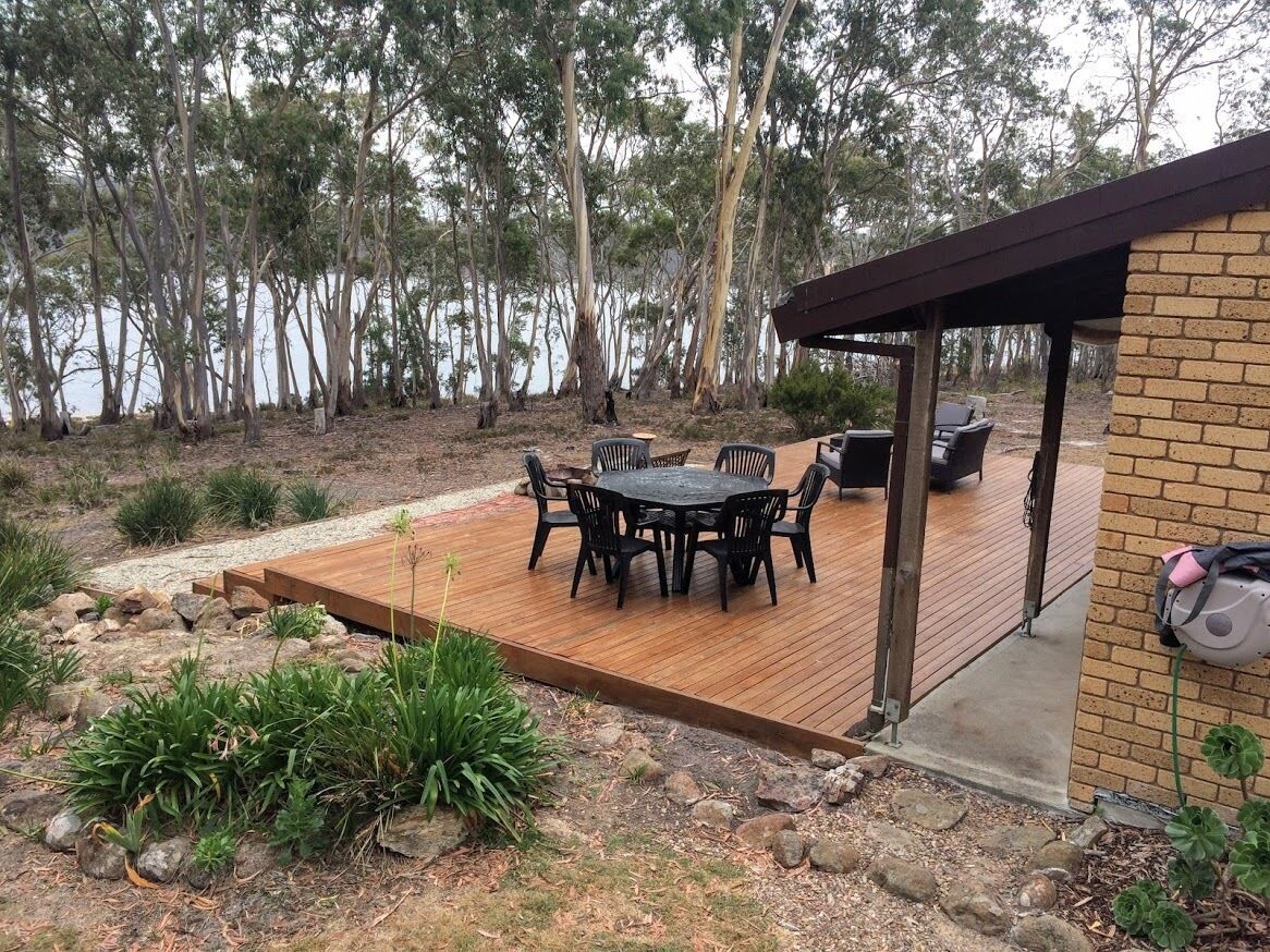 A deck with a table and chairs, surrounded by a natural landscape with trees and a body of water.
