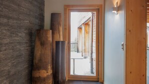 A hallway with a wooden floor, a large wooden door, and a view of a wooden building outside. - Woovim 14 by Interhome (Nendaz)