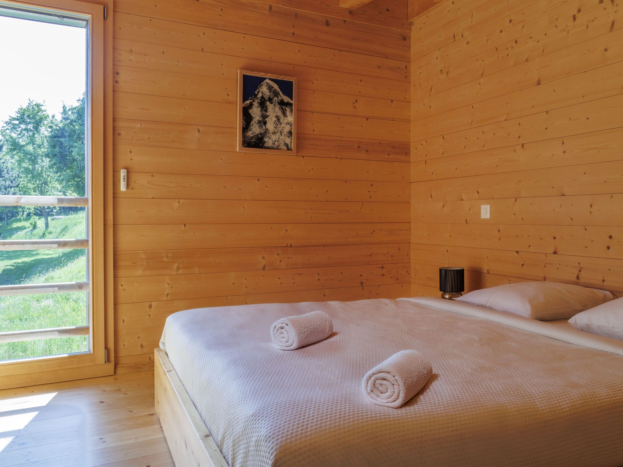 A wooden room with a bed, a small painting, and a window.