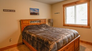 A bedroom with a wooden bed, a nightstand, a lamp, a window with blinds, a framed picture, and a sign on the wall.