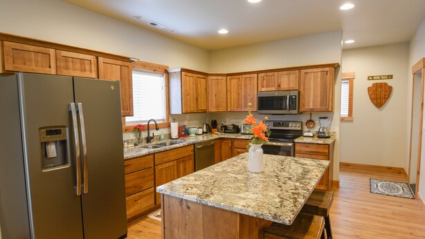 A modern kitchen with wooden cabinets, granite countertops, stainless steel appliances, and a central island with seating.