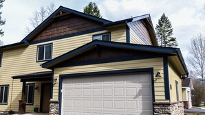 A two-story house with a garage, stone foundation, and a sloped roof.