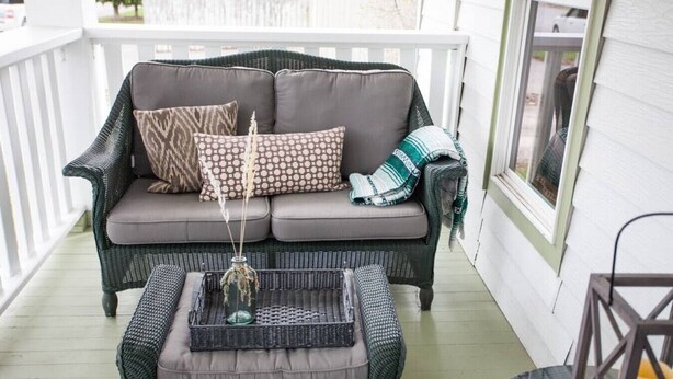 A wicker sofa with cushions and a tray table on a porch.