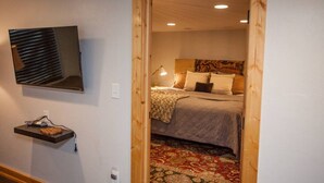 A bedroom with a bed, a bedside lamp, a TV mounted on the wall, and a wooden door.