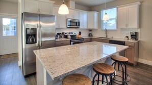 A modern kitchen with stainless steel appliances, granite countertops, and bar stools. - Beach Tripping - Oyhut Bay Seaside Village (Ocean Shores)
