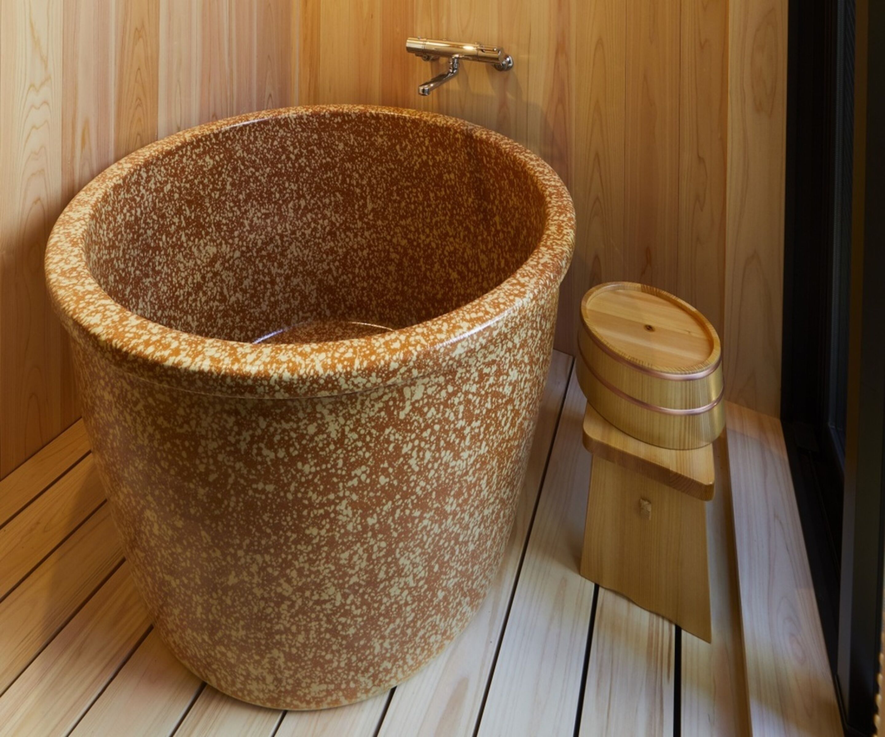 Eine große, freistehende Badewanne mit einem gemusterten Design, einem hölzernen Fußhocker und einem Metallarmaturen.
