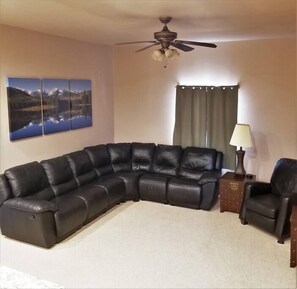Relax in this cozy living space with a large L-shaped sofa, ceiling fan, and side table.